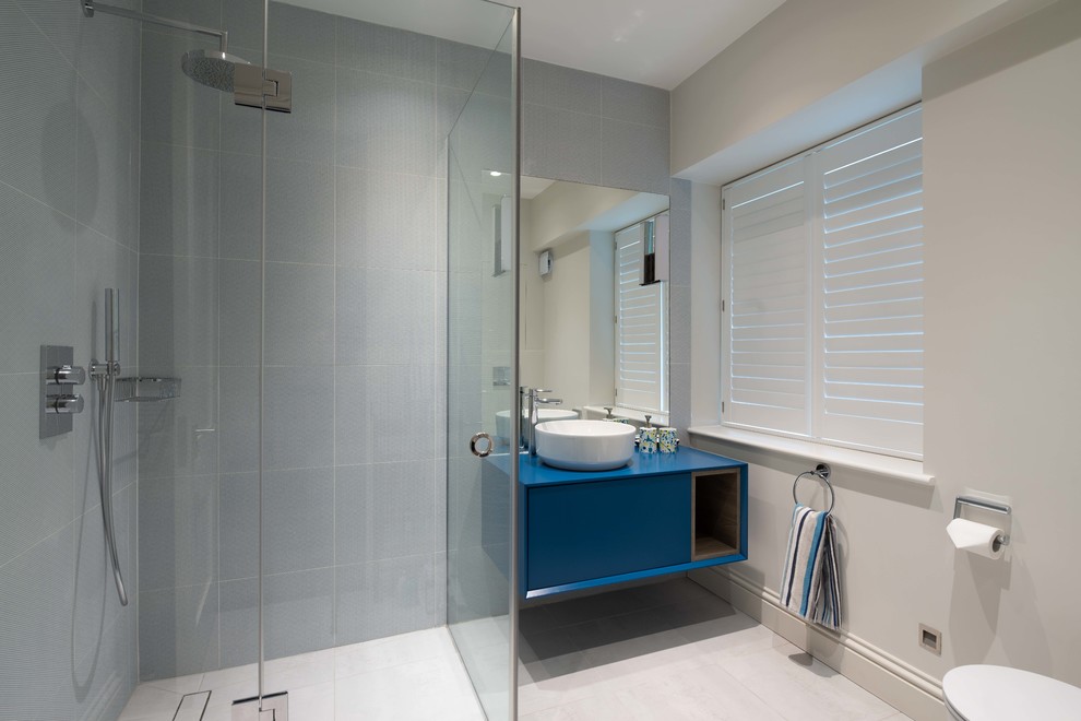 Идея дизайна: главная ванная комната среднего размера в стиле неоклассика (современная классика) с плоскими фасадами, синими фасадами, душевой комнатой, инсталляцией, синей плиткой, керамической плиткой, серыми стенами, полом из керамической плитки, подвесной раковиной, столешницей из дерева, серым полом, душем с распашными дверями и синей столешницей