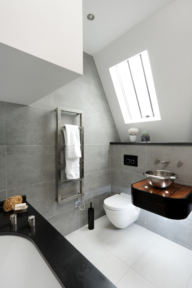 Modelo de cuarto de baño contemporáneo con lavabo sobreencimera, encimera de madera, sanitario de una pieza, baldosas y/o azulejos blancos y paredes grises