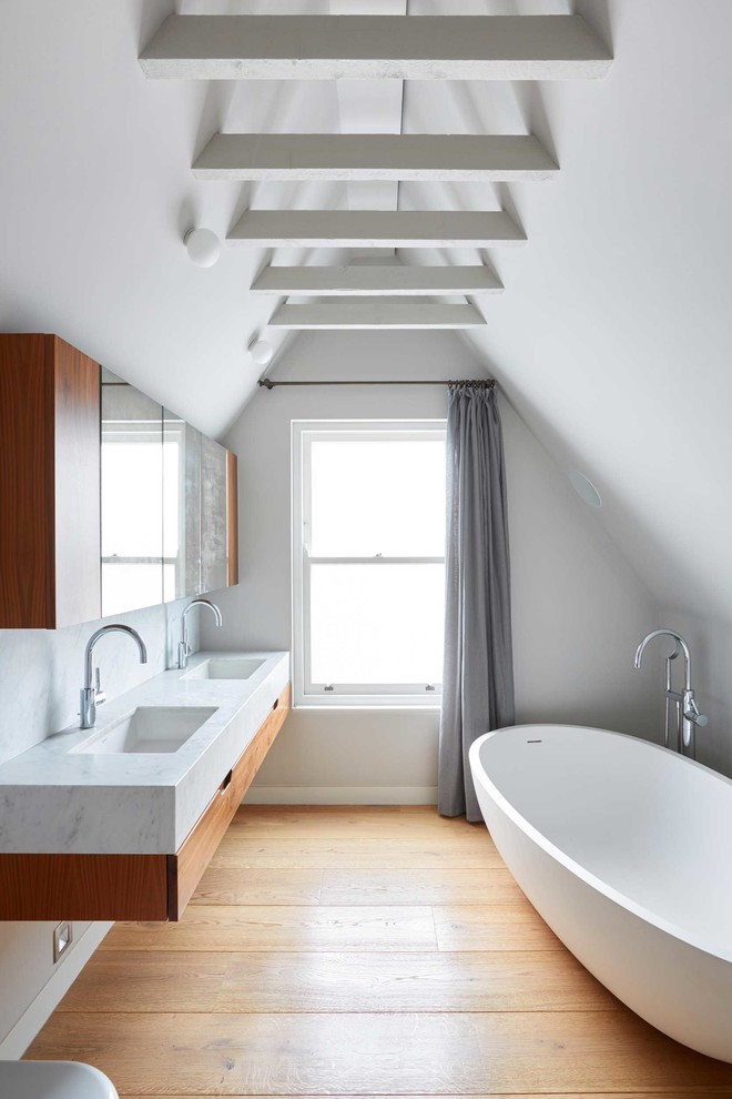 Großes Modernes Badezimmer En Suite mit hellbraunen Holzschränken, flächenbündigen Schrankfronten, freistehender Badewanne, weißer Wandfarbe, braunem Holzboden und Unterbauwaschbecken in London