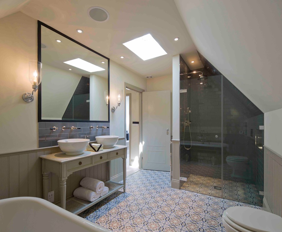 Photo of a medium sized classic ensuite bathroom in London with freestanding cabinets, beige cabinets, a claw-foot bath, a walk-in shower, a one-piece toilet, grey tiles, ceramic tiles, beige walls, mosaic tile flooring, a pedestal sink, wooden worktops, multi-coloured floors, a hinged door and white worktops.