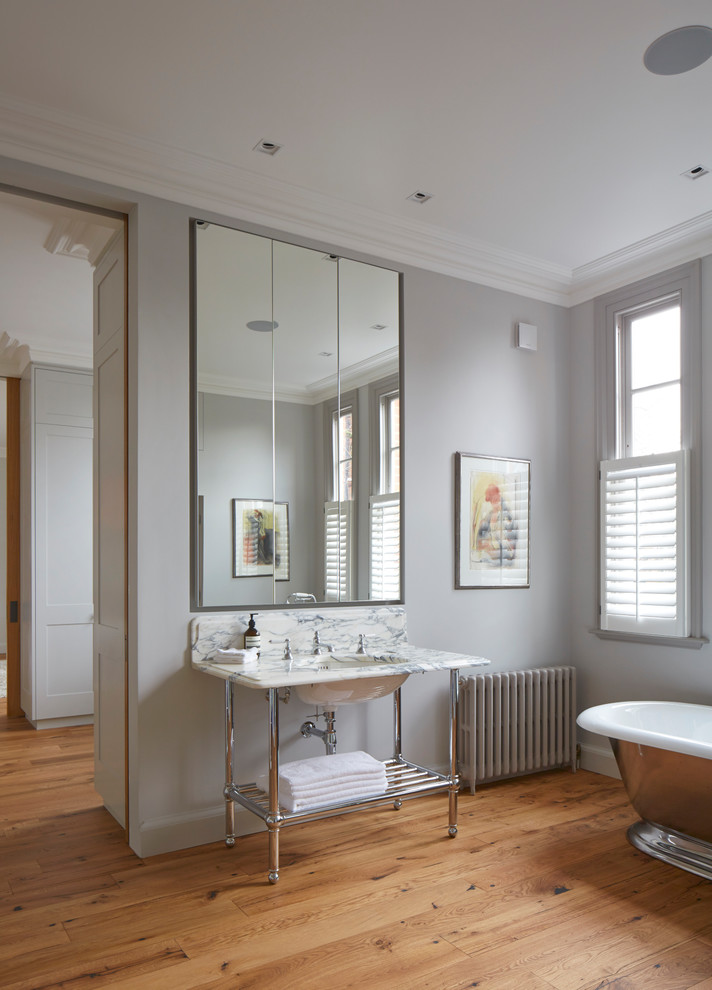 Classic bathroom in London with a freestanding bath, grey walls, medium hardwood flooring, a submerged sink, marble worktops, brown floors and white worktops.