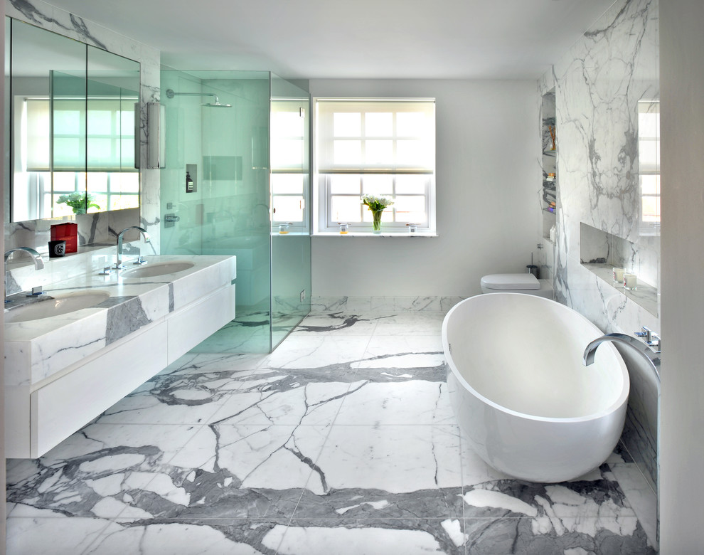 This is an example of a medium sized contemporary bathroom in London with flat-panel cabinets, white cabinets, a freestanding bath, a corner shower, marble tiles, white walls, a submerged sink and white floors.