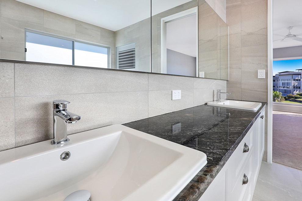 Inspiration for a large contemporary ensuite bathroom in Sunshine Coast with shaker cabinets, white cabinets, a corner bath, an alcove shower, a one-piece toilet, grey tiles, ceramic tiles, grey walls, ceramic flooring, a built-in sink, marble worktops, grey floors and black worktops.