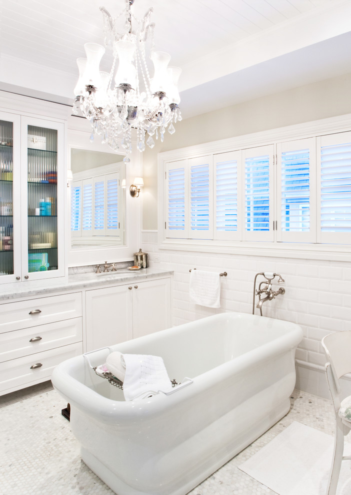 ゴールドコーストにある中くらいなトラディショナルスタイルのおしゃれな浴室 (落し込みパネル扉のキャビネット、大理石の洗面台、置き型浴槽、白いタイル、サブウェイタイル、白い壁、モザイクタイル) の写真
