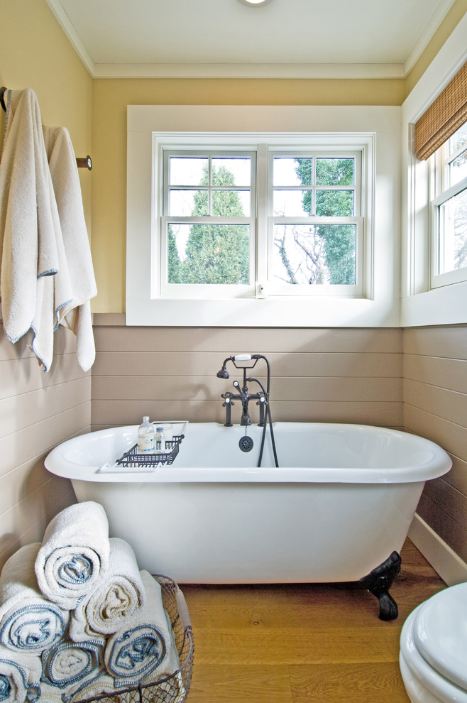 Inspiration for a coastal medium tone wood floor claw-foot bathtub remodel in New York with yellow walls