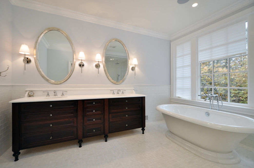 Пример оригинального дизайна: большая главная ванная комната в стиле неоклассика (современная классика) с коричневыми фасадами, отдельно стоящей ванной, душем в нише, белой плиткой, белыми стенами, настольной раковиной, мраморной столешницей, белым полом, душем с распашными дверями, белой столешницей, сиденьем для душа, тумбой под две раковины, встроенной тумбой и кессонным потолком