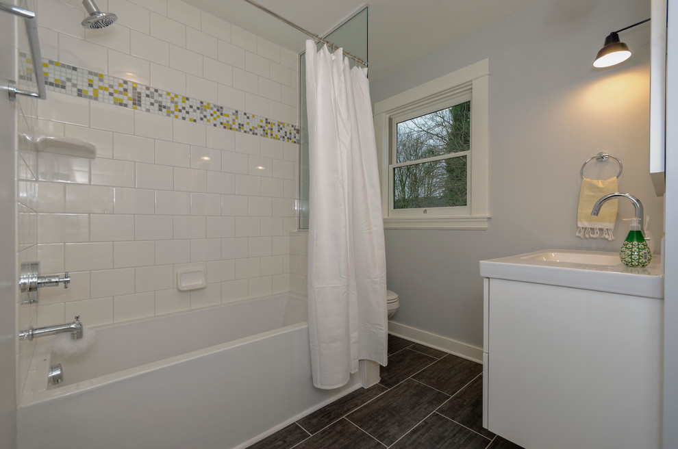 Foto på ett litet vintage badrum, med ett väggmonterat handfat, möbel-liknande, vita skåp, bänkskiva i akrylsten, ett platsbyggt badkar, en dusch/badkar-kombination, en toalettstol med separat cisternkåpa, vit kakel, keramikplattor, grå väggar och klinkergolv i keramik