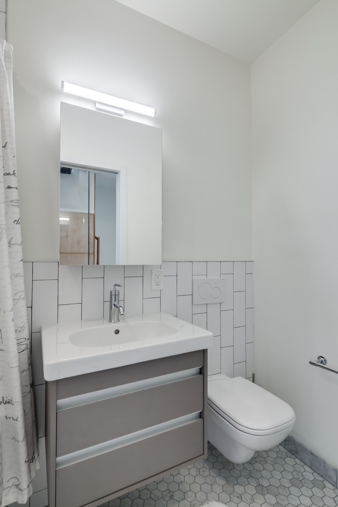 フィラデルフィアにあるお手頃価格の小さなモダンスタイルのおしゃれな浴室 (フラットパネル扉のキャビネット、茶色いキャビネット、和式浴槽、シャワー付き浴槽	、壁掛け式トイレ、白いタイル、セラミックタイル、白い壁、大理石の床、壁付け型シンク、人工大理石カウンター、白い床、シャワーカーテン) の写真