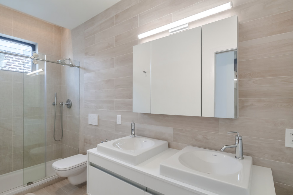 Inspiration for a small modern ensuite bathroom in Philadelphia with flat-panel cabinets, white cabinets, a wall mounted toilet, beige tiles, ceramic tiles, beige walls, ceramic flooring, a vessel sink, laminate worktops, beige floors and a sliding door.