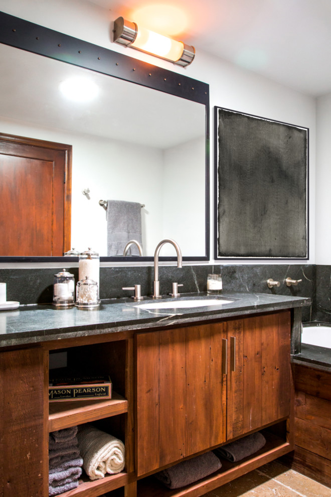 Bild på ett mellanstort industriellt en-suite badrum, med ett nedsänkt handfat, släta luckor, skåp i mellenmörkt trä, bänkskiva i täljsten, ett undermonterat badkar, vita väggar och kalkstensgolv