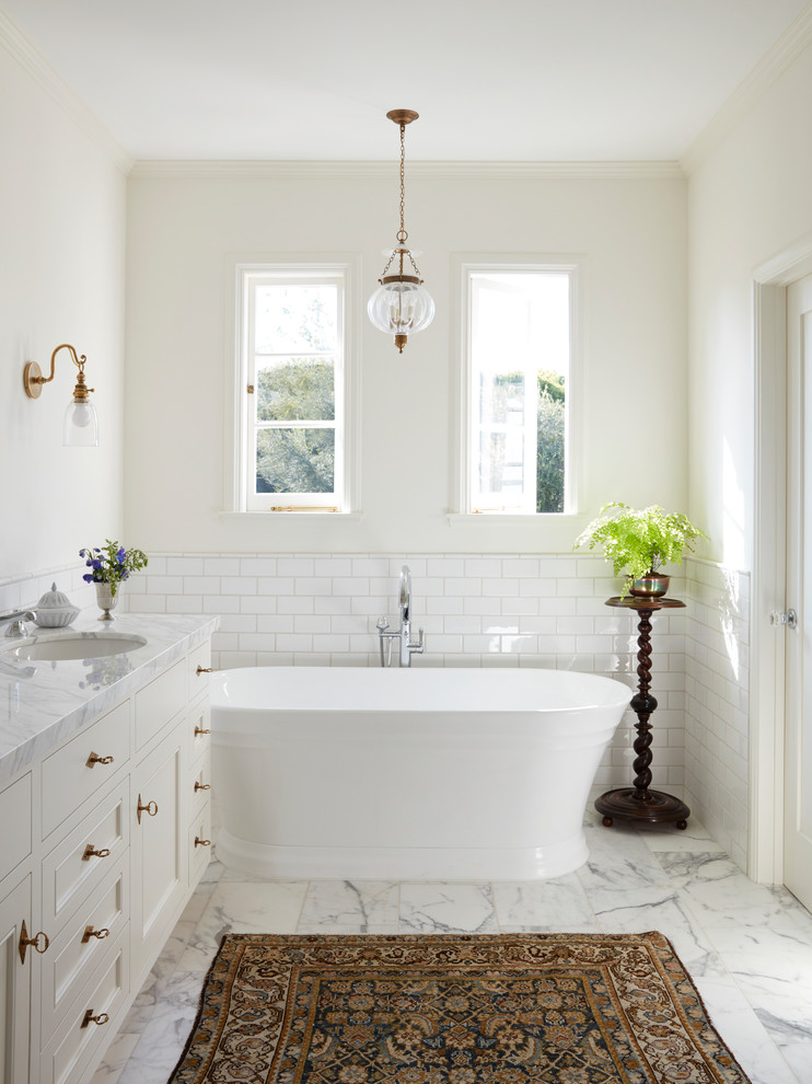 Photo of a mediterranean bathroom in Los Angeles with recessed-panel cabinets, white cabinets, a freestanding bath, white tiles, metro tiles, white walls, a submerged sink, white floors and white worktops.