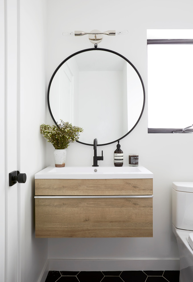 Bild på ett litet funkis vit vitt badrum med dusch, med släta luckor, skåp i ljust trä, en toalettstol med separat cisternkåpa, vita väggar, klinkergolv i keramik, bänkskiva i akrylsten, svart golv och ett konsol handfat