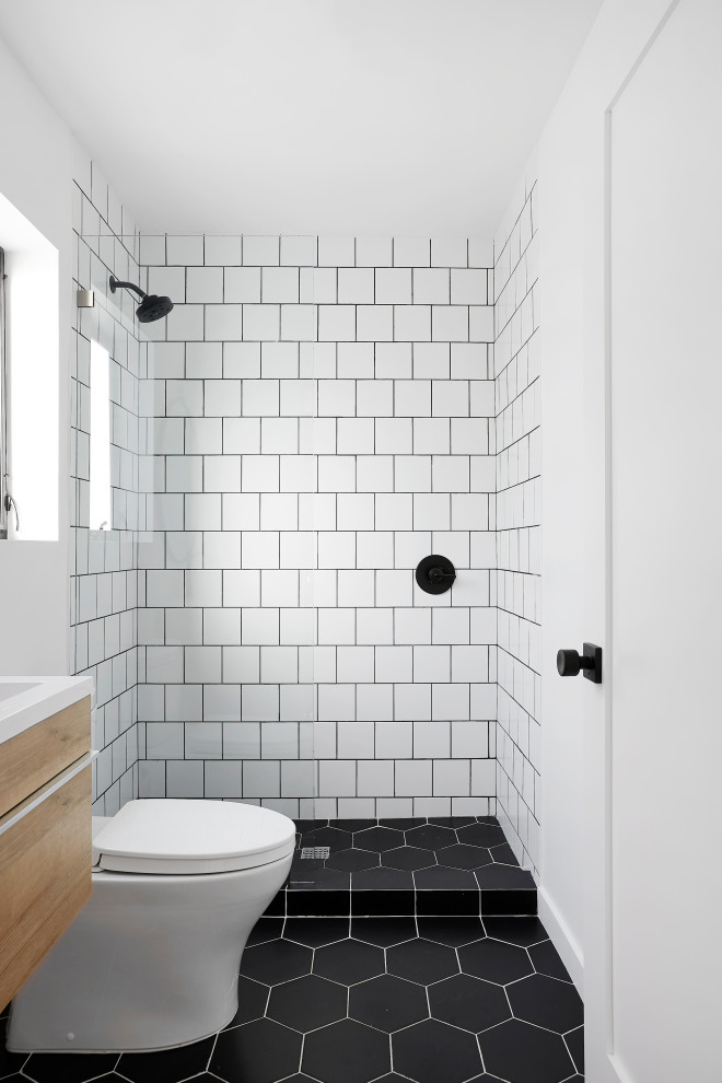 На фото: маленькая ванная комната в современном стиле с плоскими фасадами, светлыми деревянными фасадами, душем в нише, раздельным унитазом, белой плиткой, керамической плиткой, белыми стенами, полом из керамической плитки, душевой кабиной, монолитной раковиной, столешницей из искусственного камня, черным полом, открытым душем и белой столешницей для на участке и в саду с