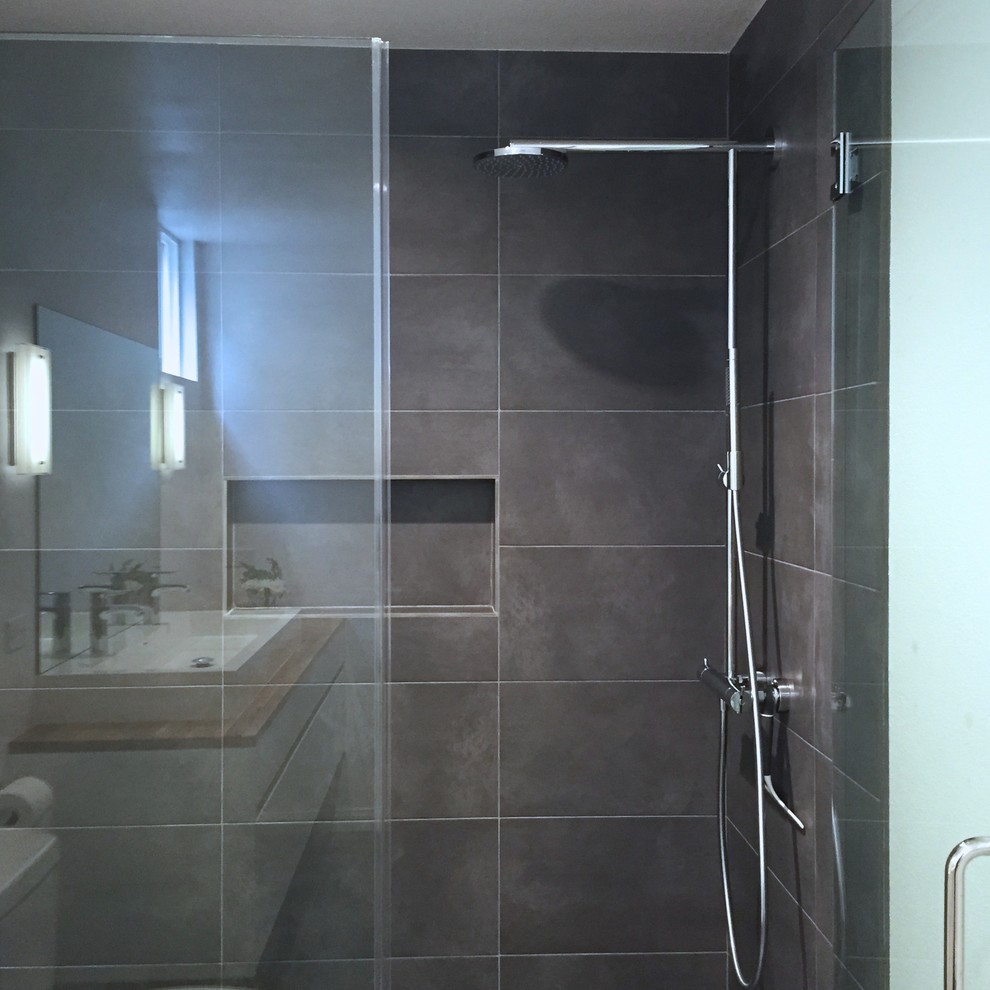 Inredning av ett skandinaviskt mellanstort badrum, med ett fristående handfat, släta luckor, vita skåp, träbänkskiva, en dusch i en alkov, grå kakel, keramikplattor, vita väggar och klinkergolv i keramik