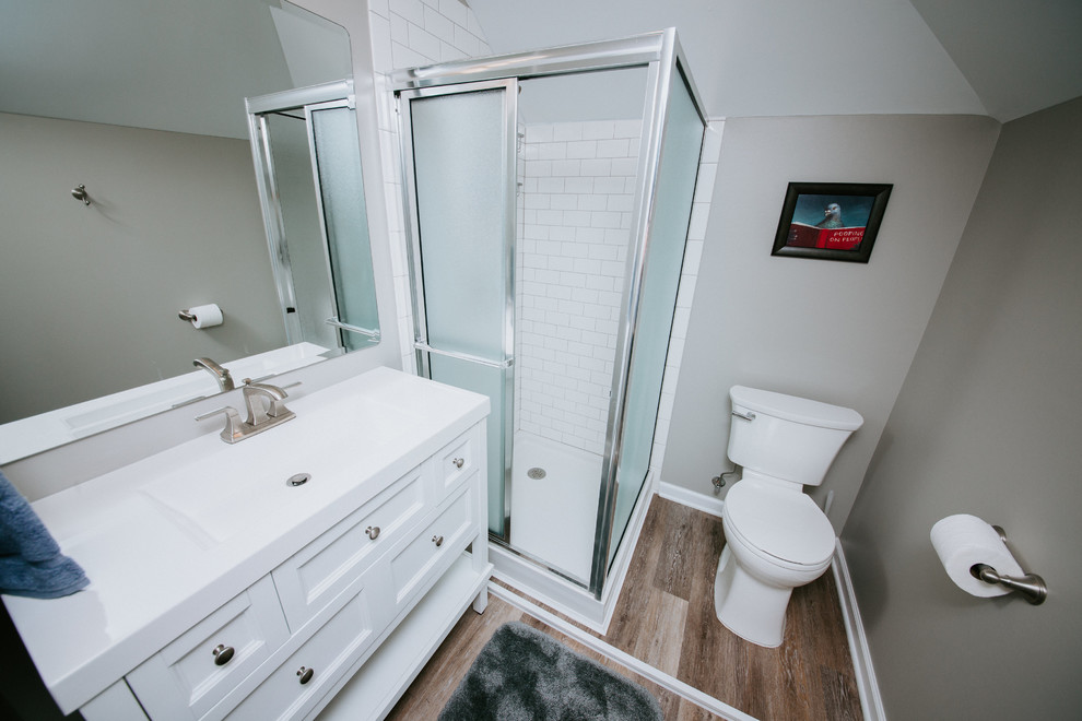 Inspiration för mellanstora klassiska vitt badrum med dusch, med luckor med infälld panel, vita skåp, en hörndusch, vit kakel, tunnelbanekakel, grå väggar, mörkt trägolv, ett integrerad handfat, bänkskiva i akrylsten, brunt golv och dusch med gångjärnsdörr