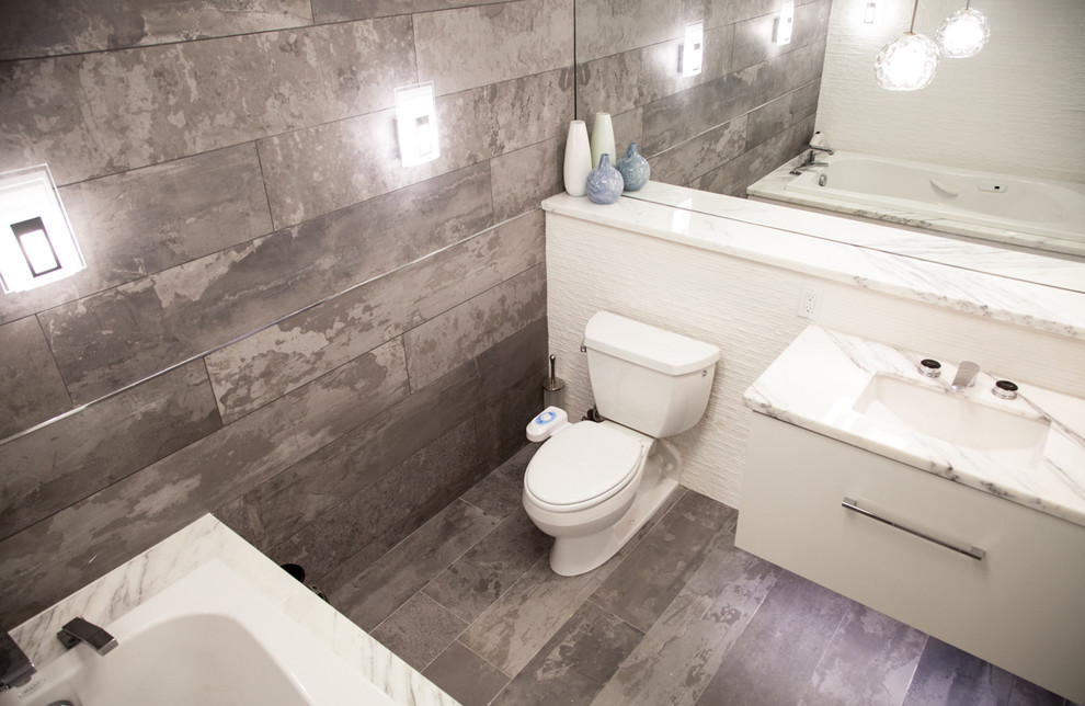 Modern inredning av ett mellanstort en-suite badrum, med ett undermonterad handfat, släta luckor, vita skåp, marmorbänkskiva, ett platsbyggt badkar, en toalettstol med separat cisternkåpa, grå kakel, porslinskakel, grå väggar och klinkergolv i porslin