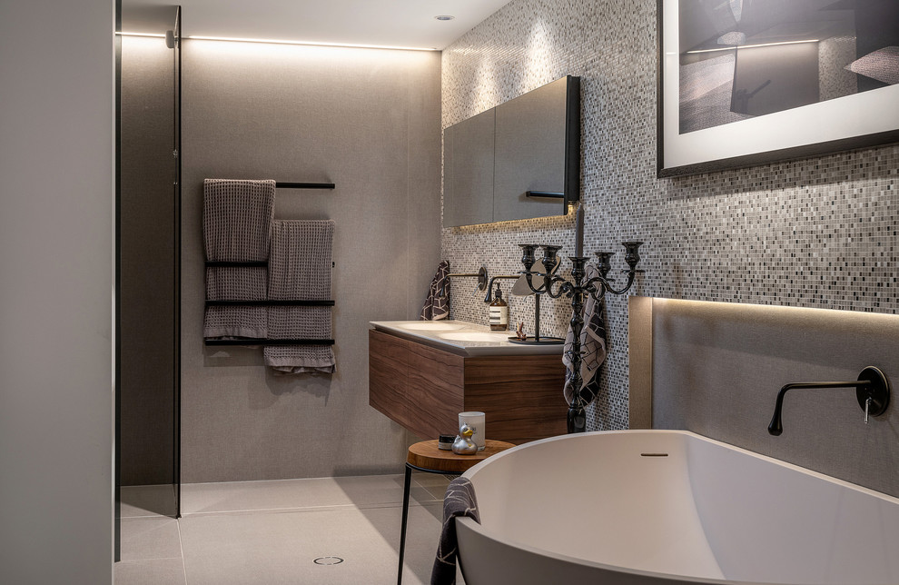 Small contemporary grey and brown ensuite bathroom in Sydney with flat-panel cabinets, dark wood cabinets, a freestanding bath, a built-in shower, grey tiles, mosaic tiles, grey walls, porcelain flooring, an integrated sink, engineered stone worktops, grey floors, white worktops and a hinged door.