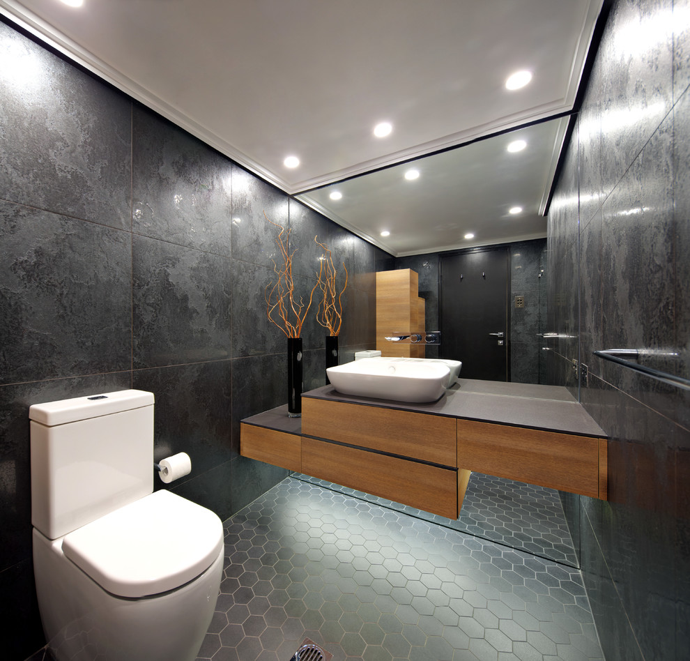Example of a mid-sized minimalist black tile ceramic tile bathroom design in Sydney with medium tone wood cabinets, a wall-mount toilet, black walls, a wall-mount sink and solid surface countertops