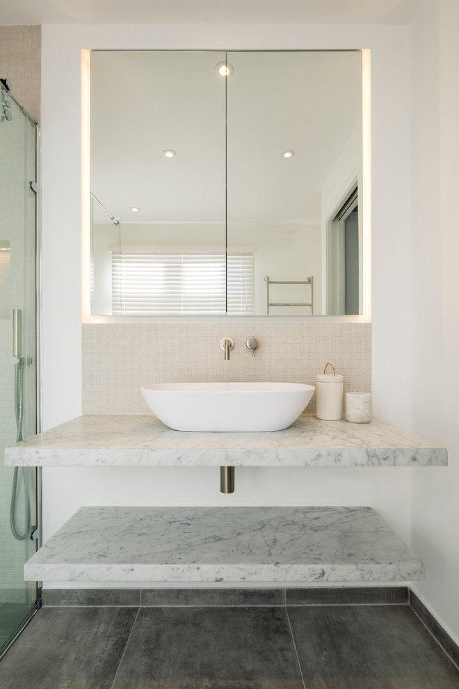 Medium sized modern ensuite bathroom in London with glass-front cabinets, a freestanding bath, a corner shower, a wall mounted toilet, beige tiles, porcelain tiles, beige walls, porcelain flooring, a vessel sink and marble worktops.