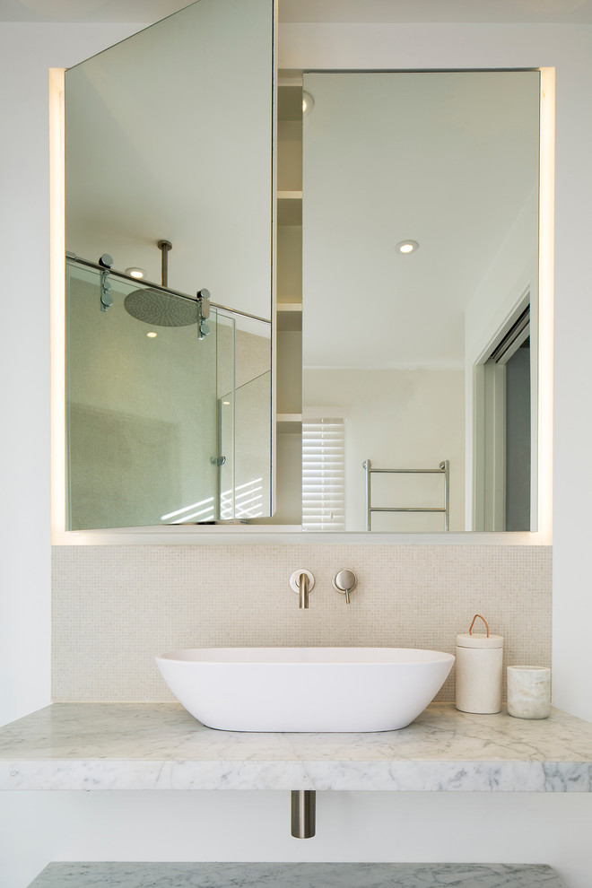 Bild på ett mellanstort funkis en-suite badrum, med luckor med glaspanel, ett fristående badkar, en hörndusch, en vägghängd toalettstol, beige kakel, mosaik, beige väggar, klinkergolv i porslin, ett fristående handfat, marmorbänkskiva och vita skåp