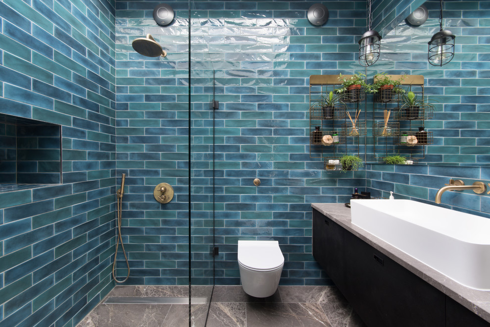 Cette image montre une salle de bain urbaine avec un placard à porte plane, des portes de placard noires, WC suspendus, un carrelage bleu, un mur bleu, une grande vasque, un sol marron et aucune cabine.
