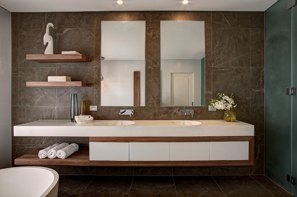 На фото: большая главная ванная комната в современном стиле с белыми фасадами, отдельно стоящей ванной, коричневой плиткой, монолитной раковиной, инсталляцией, керамогранитной плиткой, белыми стенами, полом из керамогранита и столешницей из искусственного кварца