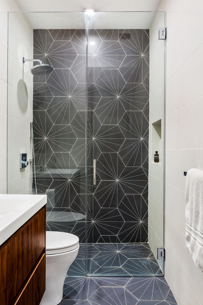 Walk-in shower - mid-sized contemporary 3/4 gray tile and porcelain tile porcelain tile, gray floor and single-sink walk-in shower idea in New York with flat-panel cabinets, medium tone wood cabinets, a one-piece toilet, white walls, an integrated sink, solid surface countertops, a hinged shower door, white countertops and a floating vanity