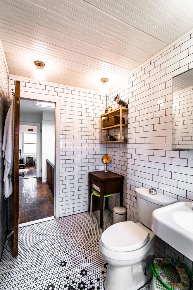 50 tals inredning av ett litet badrum, med ett badkar med tassar, en toalettstol med separat cisternkåpa, vit kakel, porslinskakel, beige väggar och ljust trägolv
