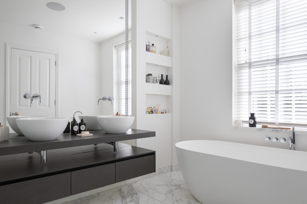 ロンドンにある中くらいなコンテンポラリースタイルのおしゃれな浴室 (フラットパネル扉のキャビネット、黒いキャビネット、置き型浴槽、白い壁、大理石の床、ベッセル式洗面器、木製洗面台、白い床、黒い洗面カウンター) の写真