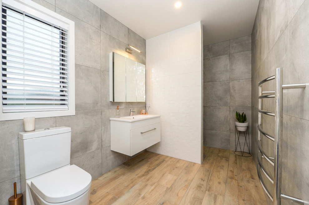 Exempel på ett modernt badrum med dusch, med släta luckor, vita skåp, våtrum, en toalettstol med hel cisternkåpa, grå kakel, grå väggar, mellanmörkt trägolv, ett integrerad handfat, beiget golv och med dusch som är öppen