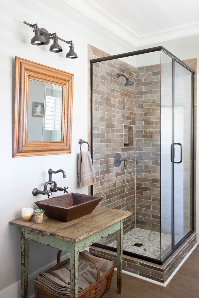 Bild på ett lantligt brun brunt badrum med dusch, med en hörndusch, tunnelbanekakel, grå väggar, mellanmörkt trägolv, ett fristående handfat, träbänkskiva, brunt golv, dusch med gångjärnsdörr, skåp i slitet trä och brun kakel