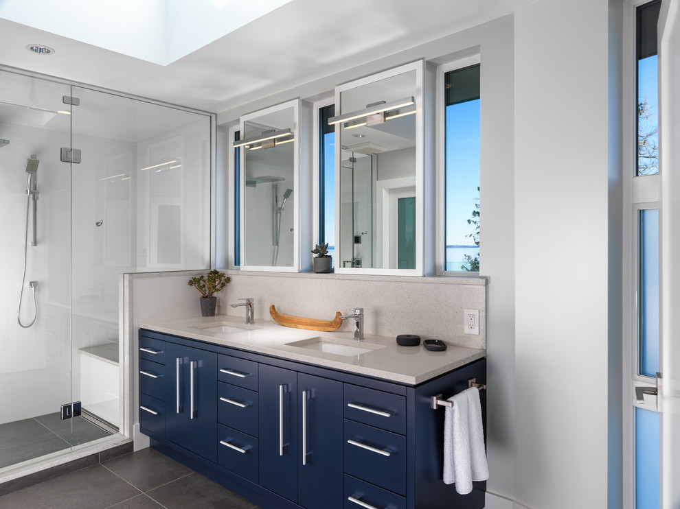 Идея дизайна: ванная комната в современном стиле с плоскими фасадами, синими фасадами, душем в нише, белой плиткой, серыми стенами, врезной раковиной, серым полом, душем с распашными дверями, бежевой столешницей и зеркалом с подсветкой
