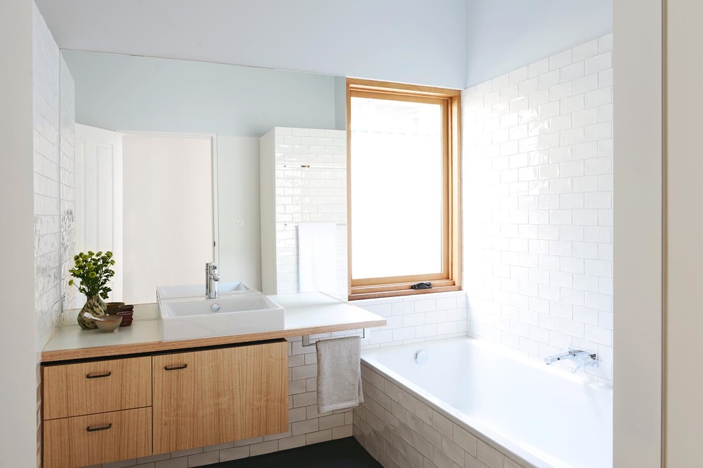 Идея дизайна: ванная комната среднего размера в скандинавском стиле с настольной раковиной, плоскими фасадами, светлыми деревянными фасадами, столешницей из ламината, ванной в нише, белой плиткой, керамической плиткой, синими стенами и полом из керамической плитки