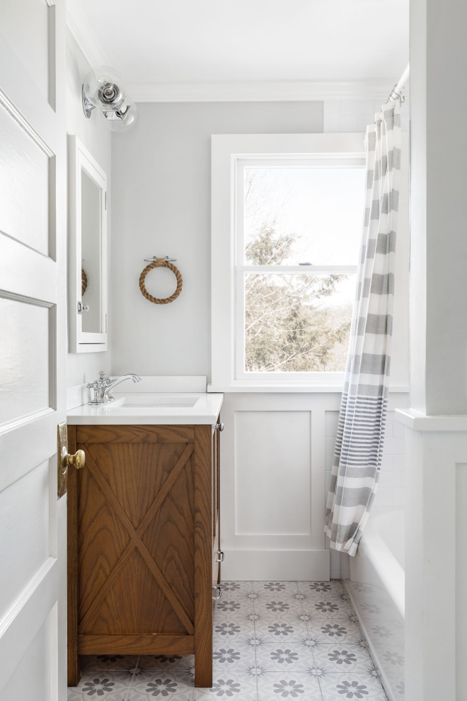 Inspiration for a traditional bathroom in New York with medium wood cabinets, an alcove bath, a shower/bath combination, grey walls, a submerged sink, grey floors, a shower curtain, white worktops, a single sink, a freestanding vanity unit and wainscoting.