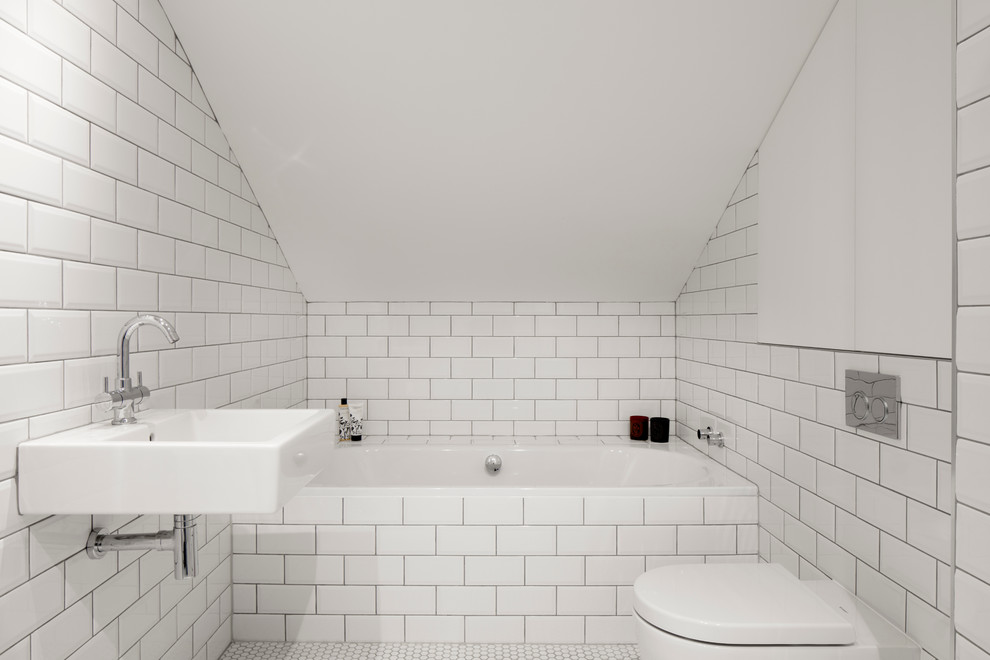 Klassisches Badezimmer mit Badewanne in Nische, Wandtoilette, Metrofliesen, weißer Wandfarbe, Mosaik-Bodenfliesen und Wandwaschbecken in London