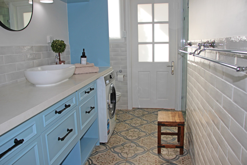 Пример оригинального дизайна: большая ванная комната в средиземноморском стиле с фасадами островного типа, синими фасадами, угловым душем, раздельным унитазом, бежевой плиткой, плиткой кабанчик, белыми стенами, полом из керамогранита, столешницей из искусственного кварца, душем с распашными дверями, бежевой столешницей, тумбой под одну раковину, встроенной тумбой и настольной раковиной