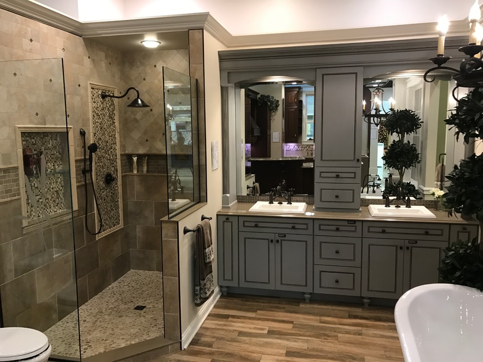 Medium sized mediterranean ensuite bathroom in Cleveland with beaded cabinets, grey cabinets, a freestanding bath, a corner shower, beige tiles, ceramic tiles, a built-in sink, solid surface worktops, a hinged door, a two-piece toilet, beige walls, medium hardwood flooring and brown floors.
