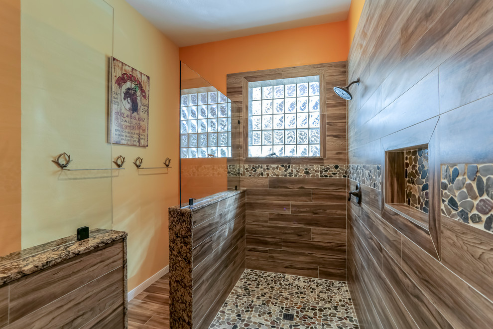 Cette image montre une grande salle de bain principale sud-ouest américain avec un placard à porte affleurante, des portes de placards vertess, une douche double, WC séparés, un carrelage marron, des carreaux de porcelaine, un mur orange, un sol en carrelage de porcelaine, un lavabo encastré et un plan de toilette en granite.