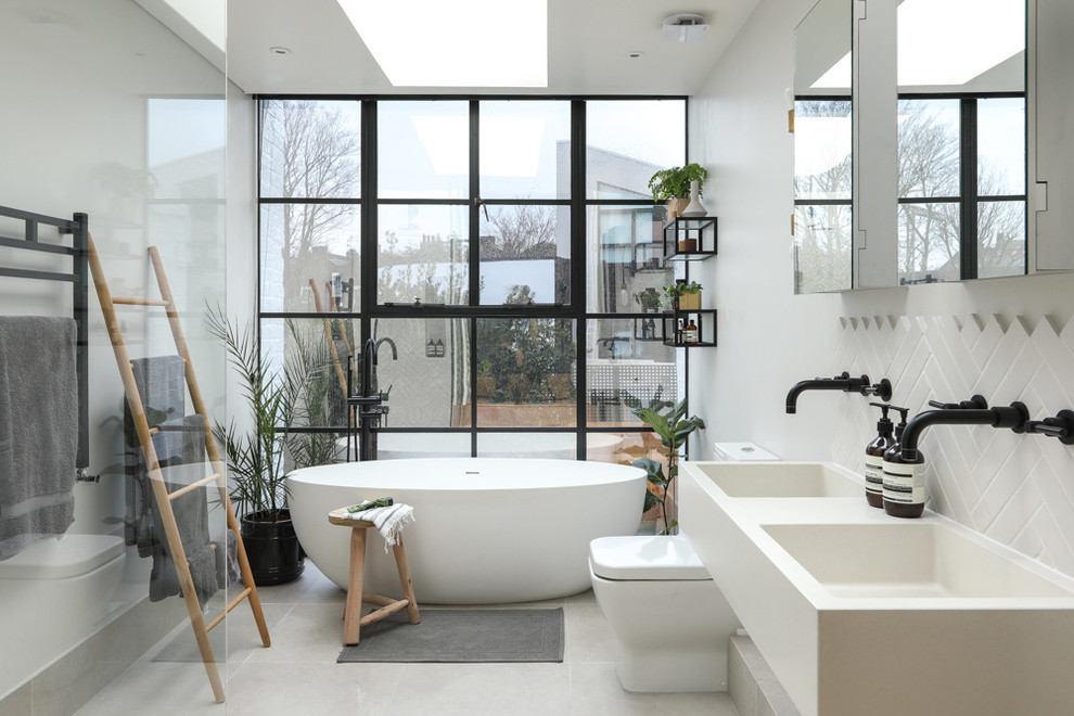 Foto på ett stort nordiskt vit badrum med dusch, med vita skåp, ett fristående badkar, en öppen dusch, en toalettstol med hel cisternkåpa, grå kakel, keramikplattor, vita väggar, klinkergolv i keramik, ett väggmonterat handfat, marmorbänkskiva, vitt golv och med dusch som är öppen