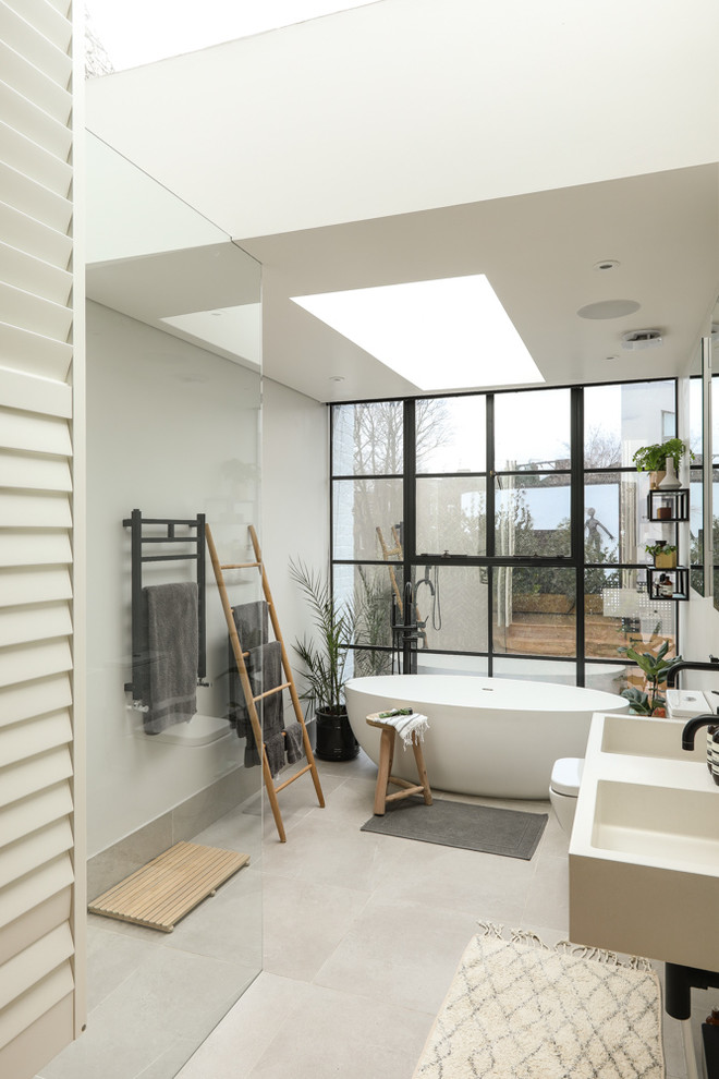 This is an example of a large scandi shower room bathroom in London with white cabinets, a freestanding bath, a walk-in shower, a one-piece toilet, grey tiles, ceramic tiles, white walls, ceramic flooring, a wall-mounted sink, marble worktops, white floors, an open shower and white worktops.