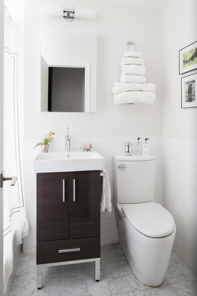 Modern inredning av ett badrum, med marmorgolv, släta luckor, skåp i mörkt trä, en toalettstol med hel cisternkåpa och vit kakel