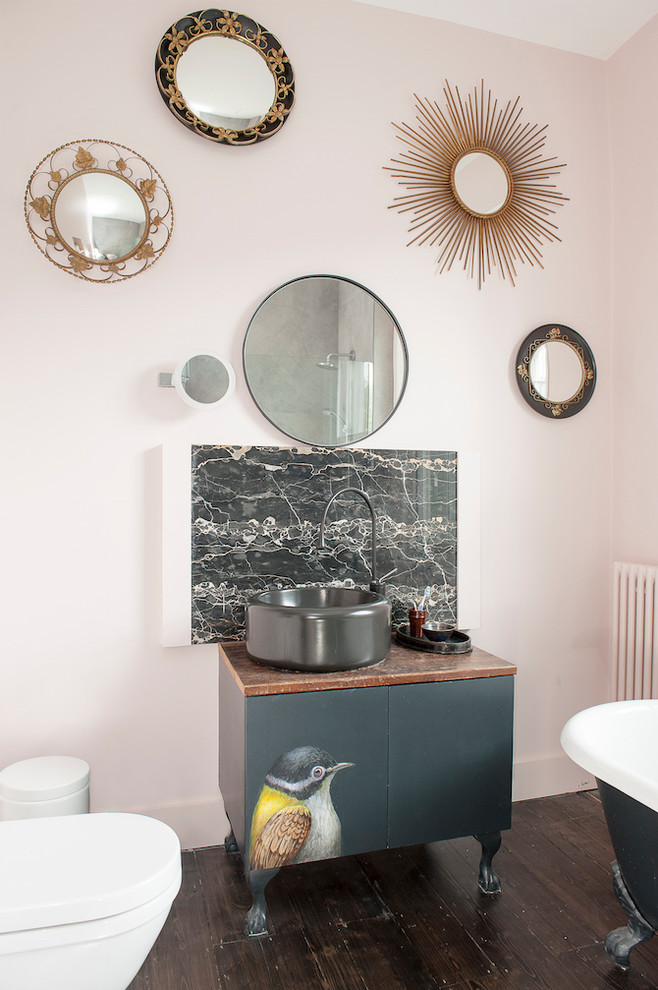 This is an example of a large bohemian family bathroom in Sussex with flat-panel cabinets, black cabinets, a claw-foot bath, stone slabs, beige walls, dark hardwood flooring, a vessel sink, wooden worktops and a one-piece toilet.