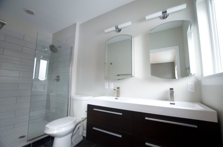 Photo of a modern ensuite bathroom in Other with an integrated sink, flat-panel cabinets, dark wood cabinets, solid surface worktops, a double shower, a two-piece toilet, grey tiles, ceramic tiles, white walls and ceramic flooring.