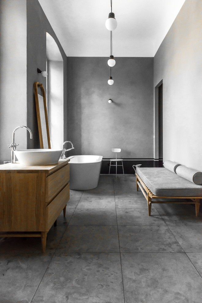 Large contemporary grey and white bathroom in Berlin with medium wood cabinets, a freestanding bath, an alcove shower, a wall mounted toilet, grey tiles, porcelain tiles, grey walls, porcelain flooring, a vessel sink, wooden worktops and flat-panel cabinets.