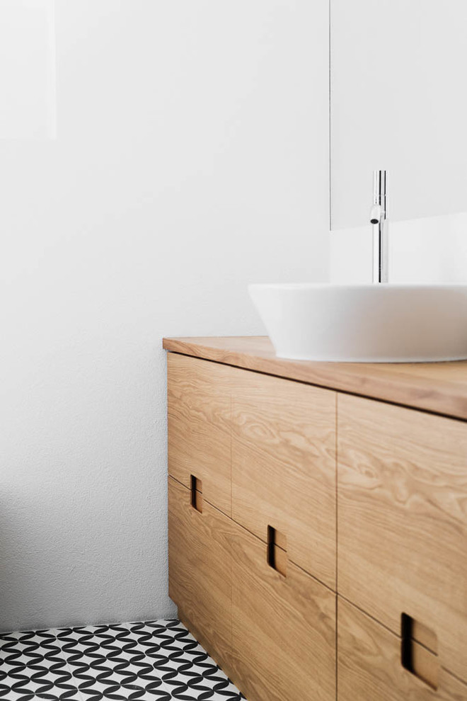 This is an example of a medium sized scandi ensuite bathroom in Other with flat-panel cabinets, medium wood cabinets, a freestanding bath, a wall mounted toilet, black and white tiles, ceramic tiles, white walls, ceramic flooring, a vessel sink and wooden worktops.