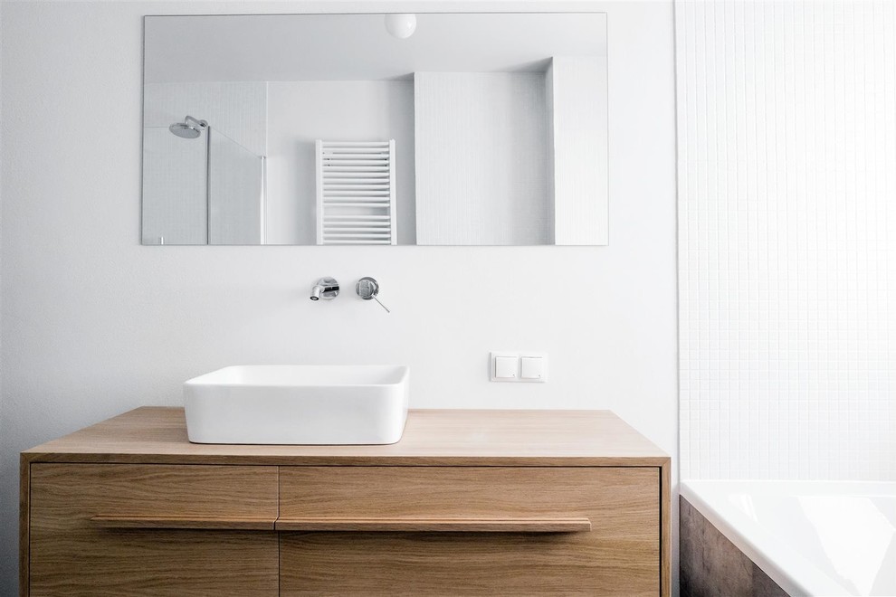 Photo of a medium sized contemporary ensuite bathroom in Berlin with freestanding cabinets, medium wood cabinets, a built-in bath, a built-in shower, a wall mounted toilet, grey tiles, ceramic tiles, white walls, ceramic flooring, a vessel sink and wooden worktops.