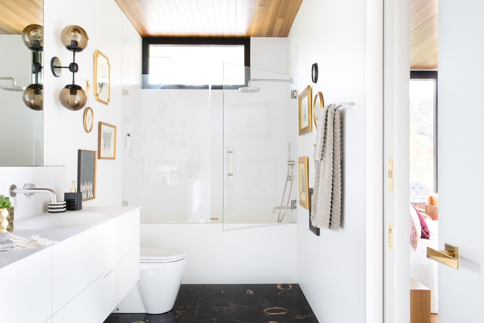 Foto på ett funkis badrum med dusch, med släta luckor, vita skåp, ett badkar i en alkov, en dusch/badkar-kombination, vita väggar, ett integrerad handfat, svart golv och dusch med gångjärnsdörr