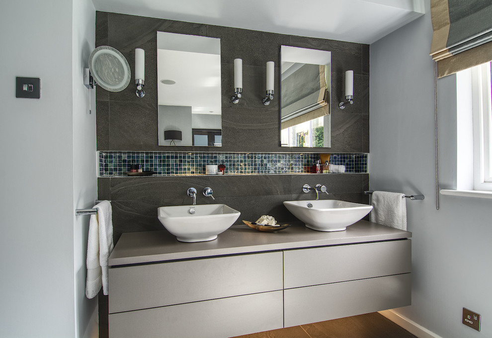 Modern inredning av ett mellanstort en-suite badrum, med släta luckor, grå skåp, grå kakel, keramikplattor, grå väggar, klinkergolv i keramik, ett konsol handfat, laminatbänkskiva och grått golv