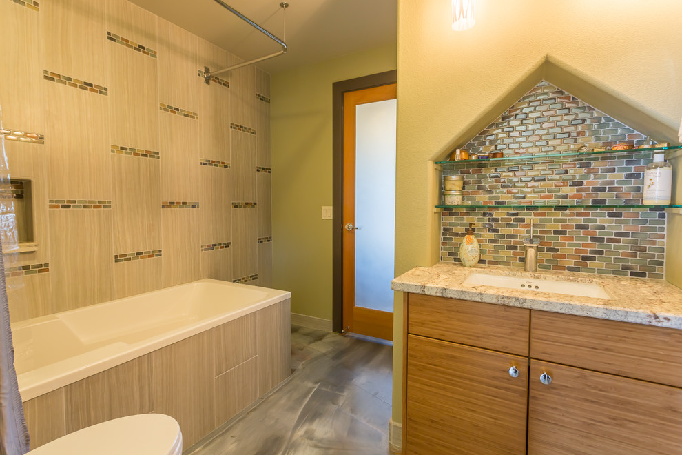 Example of a mid-sized 1960s kids' gray tile and glass sheet concrete floor corner bathtub design in Other with an undermount sink, flat-panel cabinets, medium tone wood cabinets, granite countertops and green walls