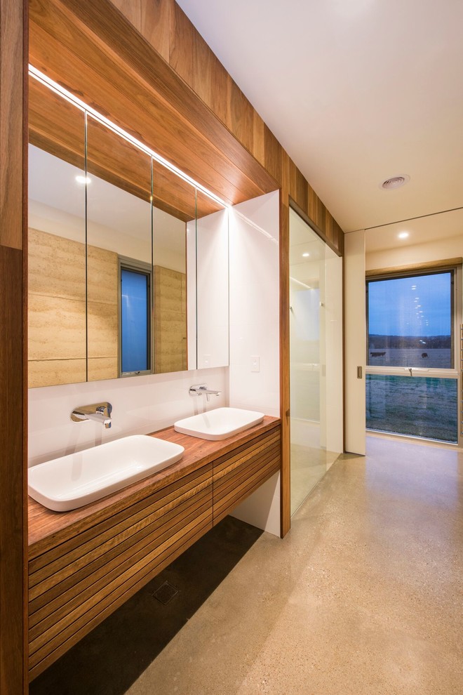 Exempel på ett modernt brun brunt badrum, med släta luckor, skåp i mellenmörkt trä, en kantlös dusch, vit kakel, vita väggar, betonggolv, ett nedsänkt handfat, träbänkskiva, grått golv och dusch med gångjärnsdörr